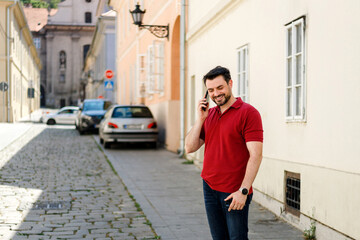 Fototapeta premium Man smiles while talking on phone in a charming cobblestone street during the day