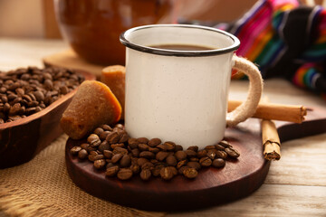 Cafe de Olla. Traditional Mexican coffee and basic ingredients for its preparation, coffee, cinnamon and piloncillo, served in a metallic cup called "peltre" on a rustic wooden surface.