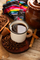 Cafe de Olla. Traditional Mexican coffee and basic ingredients for its preparation, coffee, cinnamon and piloncillo, served in a metallic cup called "peltre" on a rustic wooden surface.