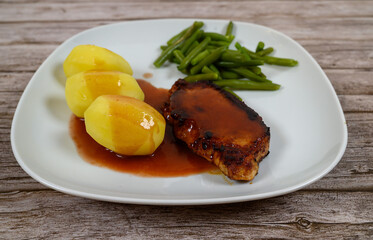 A well-prepared meal features a pork chop covered in gravy alongside three steamed potatoes and a serving of green beans on a rustic wooden table