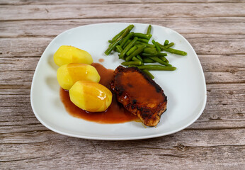 A well-prepared meal features a pork chop covered in gravy alongside three steamed potatoes and a serving of green beans on a rustic wooden table