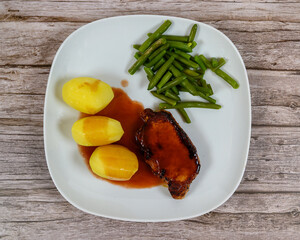 A well-prepared meal features a pork chop covered in gravy alongside three steamed potatoes and a serving of green beans on a rustic wooden table