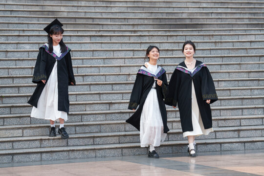 three happy asian graduates walking down the steps in the campus