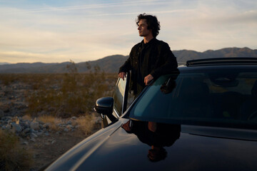 Man Leans on Car While Enjoying Sunset in Desert Landscape