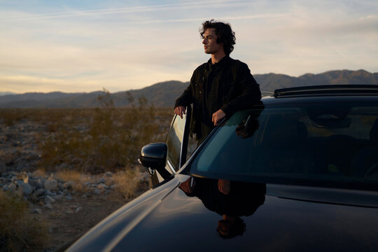 Man Leans on Car While Enjoying Sunset in Desert Landscape