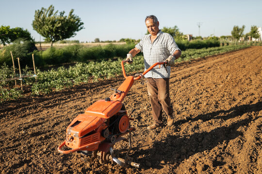 senior man tilling soil with electric cultivator