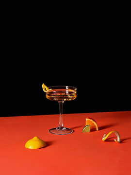 Elegant Cocktail Glass with Citrus Garnishes on Vibrant Red Background