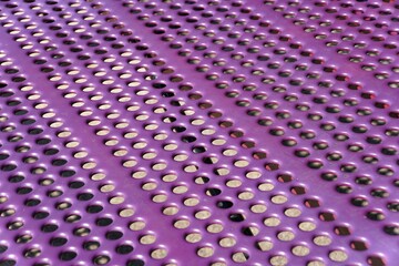 Purple metal panel with repeating patterns of oval holes.
