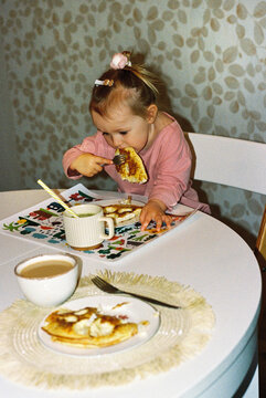 Little girl eating omelette at dining table.