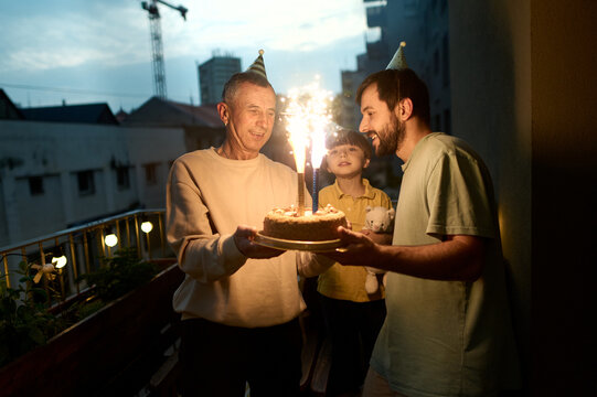 Family celebrating birthday with cake and sparklers on balcony