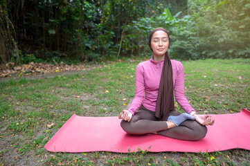 Indonesian southeast asian woman in a sporty outfit relaxing and meditating zen-like on a fitness mat in a public park outdoors. Concept of a Healthy active lifestyle