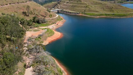 Obraz premium Impressionante paisagem aérea de barragem rodeada por colinas verdes e céu azul, perfeita para projetos turísticos e naturais.