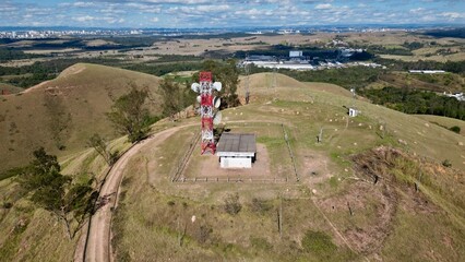 Antena de telecomunicações em destaque sobre colinas verdes e céu limpo, simbolizando a conexão...