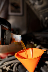 A close-up of motor oil being poured into a vehicle engine through an orange funnel, illustrating automotive repair and service.