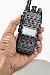 Closeup view of a human hand holding a black walkie talkie radio communication device isolated over a white background