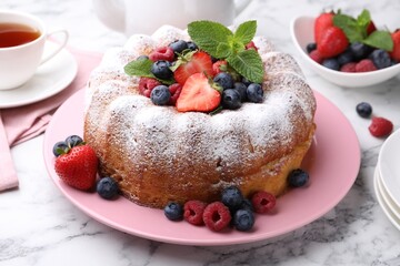 Tasty Bundt cake with powdered sugar and berries on white marble table, closeup