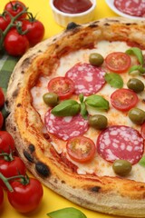 Delicious pizza with salami, olives, tomatoes and basil on yellow table, closeup