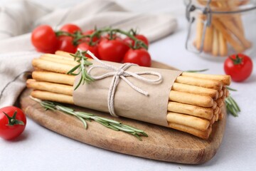 Delicious grissini sticks, rosemary and fresh tomatoes on light table, closeup