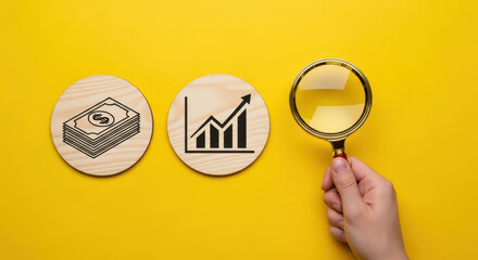 Financial Analysis Concept A Magnifying Glass Inspecting Symbols of Money and Growth on Wooden Discs Against a Bright Yellow Background