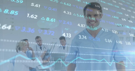 Standing smiling male doctor wearing light blue scrubs in clinic, with financial graph overlay