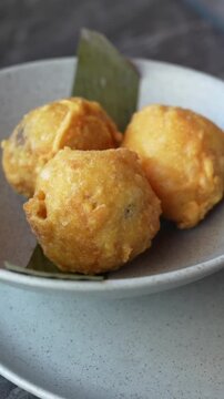 Crisp, golden brown papa rellena served on a neutral plate, lit with warm, natural lighting. This vertical video captures a close-up shot ideal for mobile and social media.