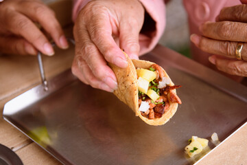 Detail of the hands of an unrecognizable elderly woman eating tacos al pastor