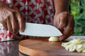 Indonesian woman hand slicing garlic on solid wooden cutting board, shot with shallow depth of field	