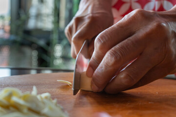 Indonesian woman hand slicing garlic on solid wooden cutting board, shot with shallow depth of field	