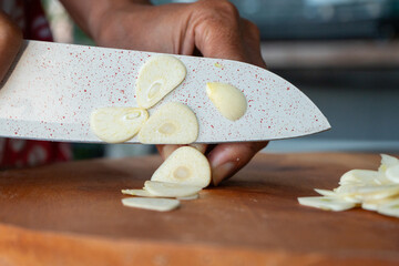 Indonesian woman hand slicing garlic on solid wooden cutting board, shot with shallow depth of field	