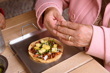 Detail of the hands of an unrecognizable elderly woman eating tacos al pastor