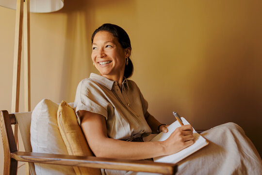 Fototapeta Smiling woman writing on notebook sitting on armchair at office
