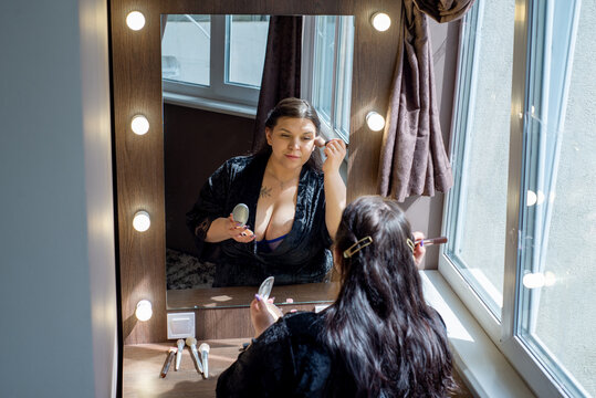Curvy woman doing makeup looking in the mirror