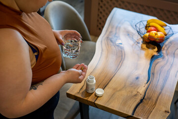 plus size  woman takes vitamin. Top view of glass of water and pills