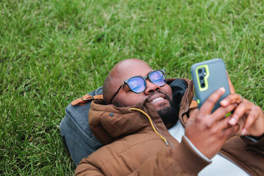 Black Man Lying on the Grass and Using Mobile Phone