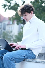 male student with coffee to go sitting in park and using laptop