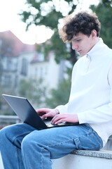 male student with coffee to go sitting in park and using laptop