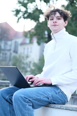 male student with coffee to go sitting in park and using laptop