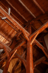A vertical shot looking up at the complex and intricate pattern of exposed wooden beams and rafters in the ceiling of a rustic cabin or cottage.