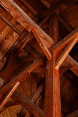 A vertical shot looking up at the complex and intricate pattern of exposed wooden beams and rafters in the ceiling of a rustic cabin or cottage.