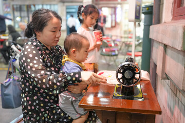 Inside an old-town mall, a Chinese family enjoys the day: a one-year-old in a stroller, kids under 10 laugh and chat as adults in their thirties use a vintage sewing machine. Shanghai, China. Spring.
