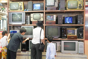 In an old-town-style mall, a Chinese family enjoys the day; a one-year-old in a stroller and kids under ten chat as adults in their thirties gather to watch old televisions. Shanghai, China. Spring.