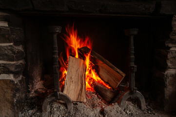 A warm fire with flames and glowing logs burning inside a large rustic fireplace made of stacked...