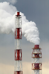 Tall red and white industrial smokestacks release white smoke into a cloudy sky, highlighting modern factory infrastructure and environmental themes.