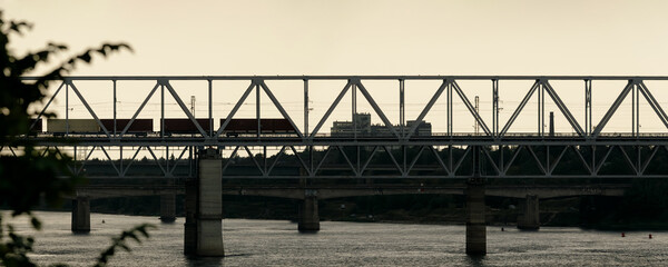 Scenic Volkhov River scene: railway bridge and passing train, industrial chimneys and lush green...