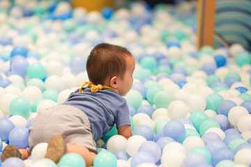 Obraz premium In an indoor play area, a one-year-old Chinese baby plays as if swimming in a pool of plastic balls. Hongkou District, Shanghai, China. Spring.