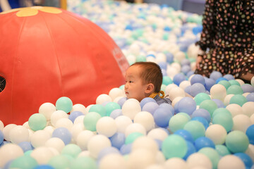 Obraz premium In an indoor play area, a one-year-old Chinese baby plays as if swimming in a pool of plastic balls. Hongkou District, Shanghai, China. Spring.