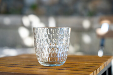 A clear, textured glass sits on a wooden table, catching sunlight and casting intricate reflections. the scene conveys a sense of tranquility and simplicity.