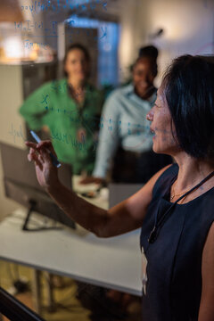 Team collaborates, writing equations on glass board.