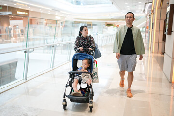 Parents in their 30s walk through a shopping mall with their 1 year old baby in a stroller. Hongkou...