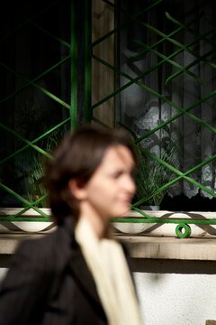 Woman walking past a green metal grid window OOF